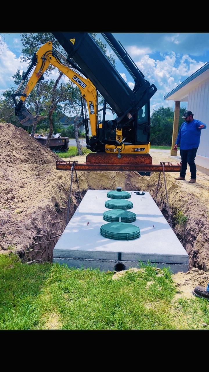 Excavator lowering a new septic tank into place at a Coastal Bend home
